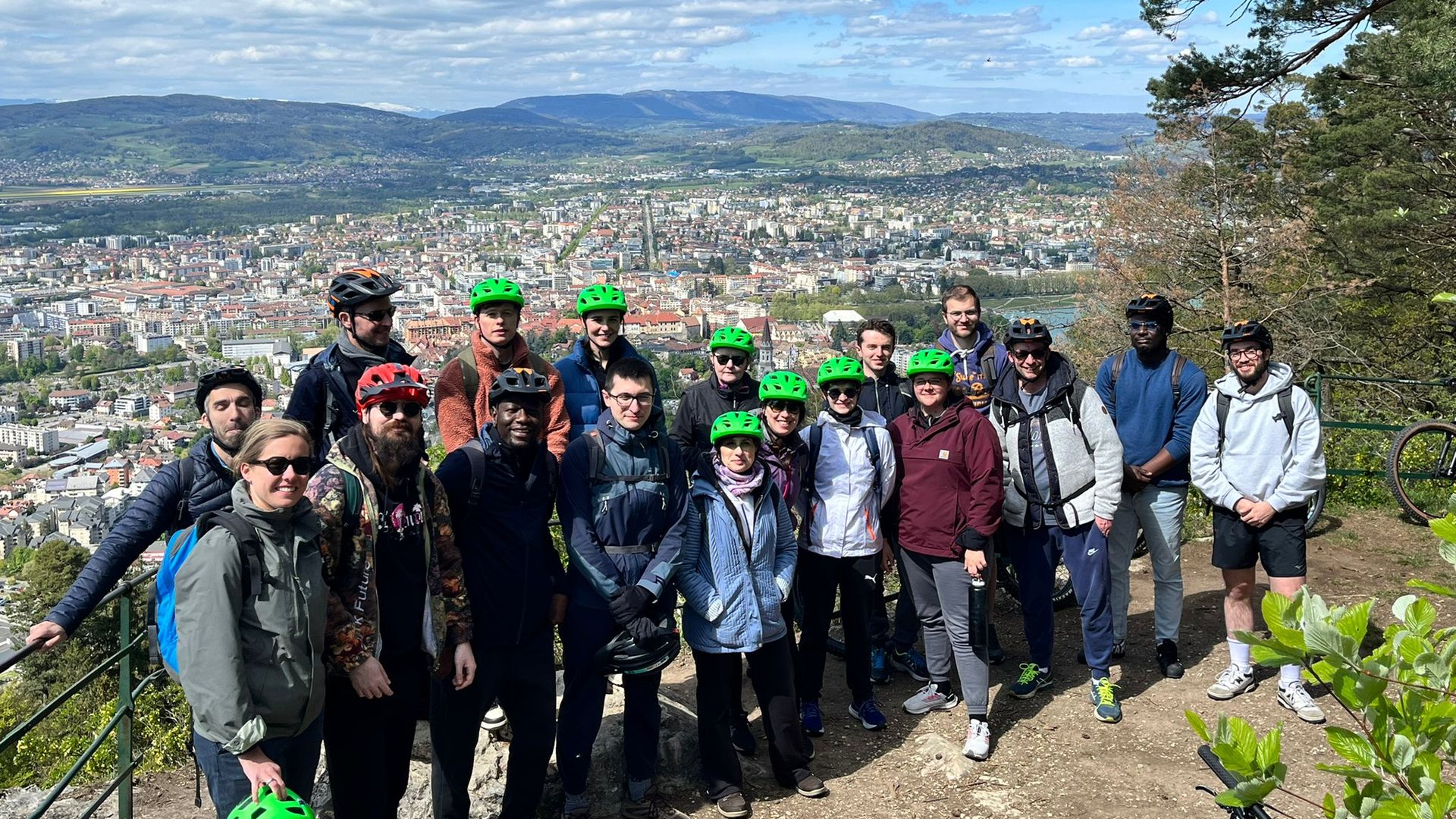 Collaborateurs en casques de vélo réunis sur un belvédère ensoleillé, au-dessus d'une ville entourée de montagnes, pendant un séminaire organisé par Weevup