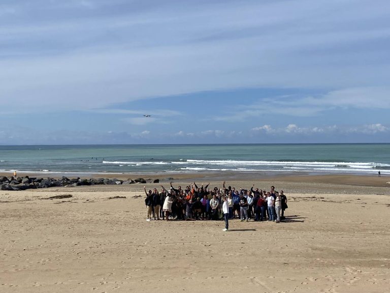 Les équipes de Libon réunies bras levés sur une grande plage du Pays basque, face à l’océan