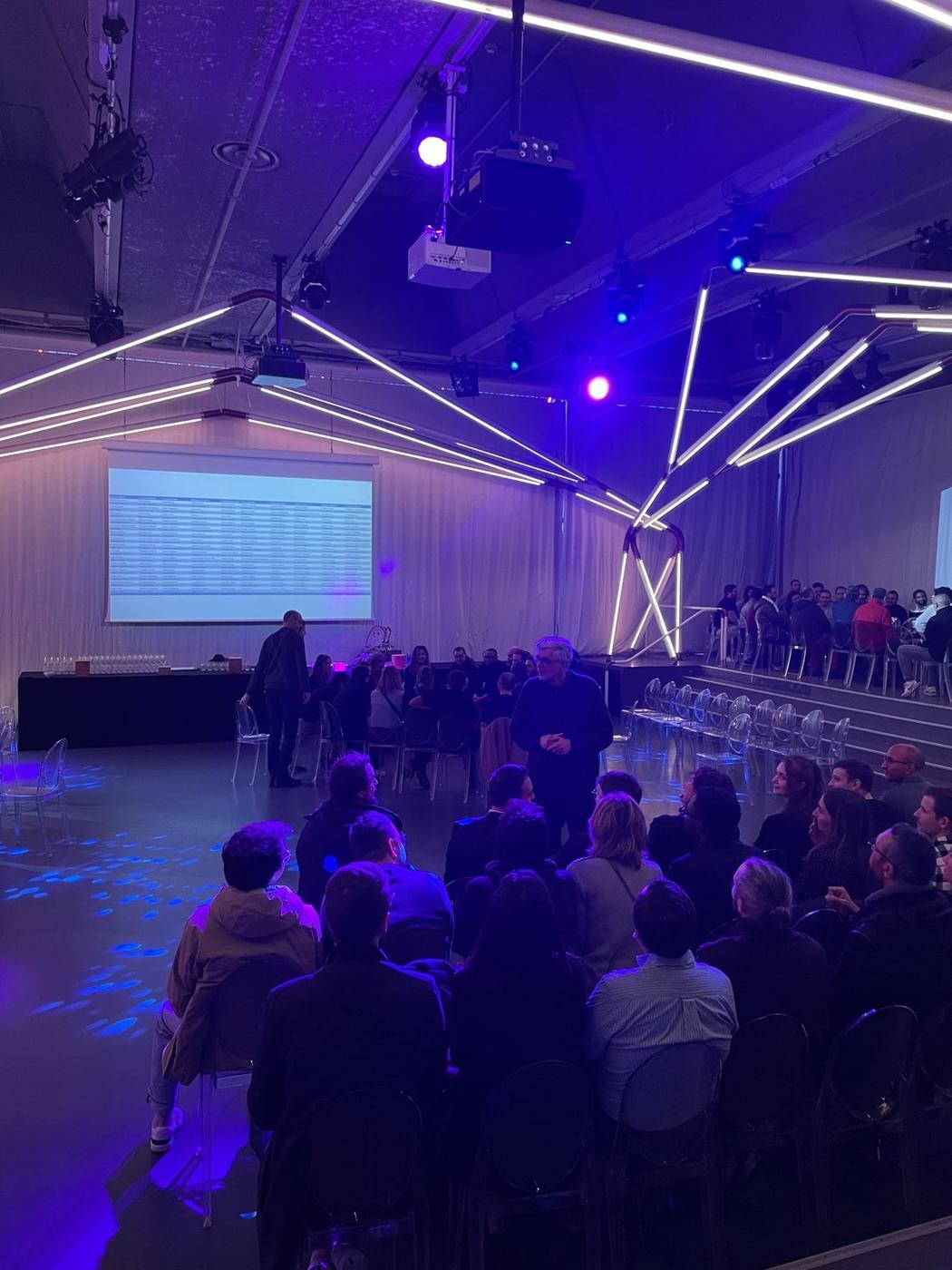 Participants de la convention annuelle 3DS Outscale assis face à un écran, sous des tubes lumineux et des éclairages violets, dans la salle privatisée par Weevup