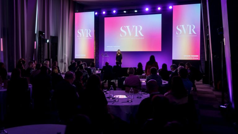 Plénière en tables rondes : une intervenante sur scène devant trois écrans aux couleurs de SVR, face aux managers réunis pour le séminaire organisé par Weevup