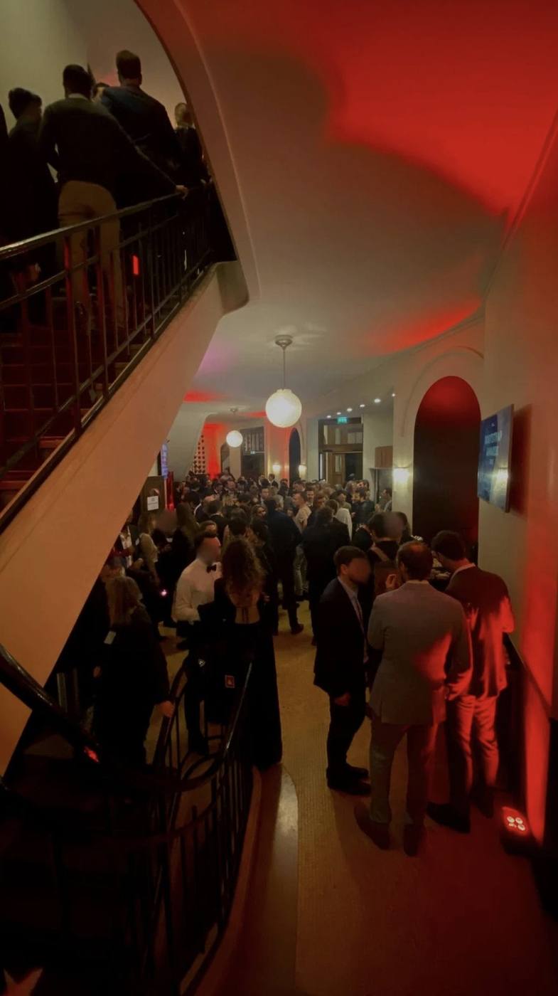 Invités du Club Boostrap réunis dans un hall historique baigné de lumière rouge, au pied d'un grand escalier, pendant la soirée organisée par Weevup