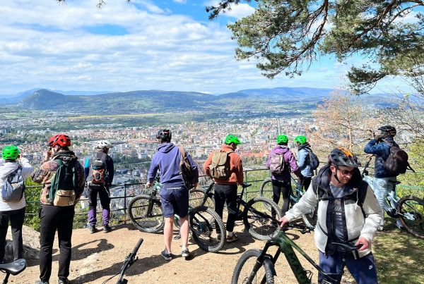 Groupe de participants d'un séminaire organisé par Weevup, en sortie VTT, face à un panorama sur une ville entourée de montagnes