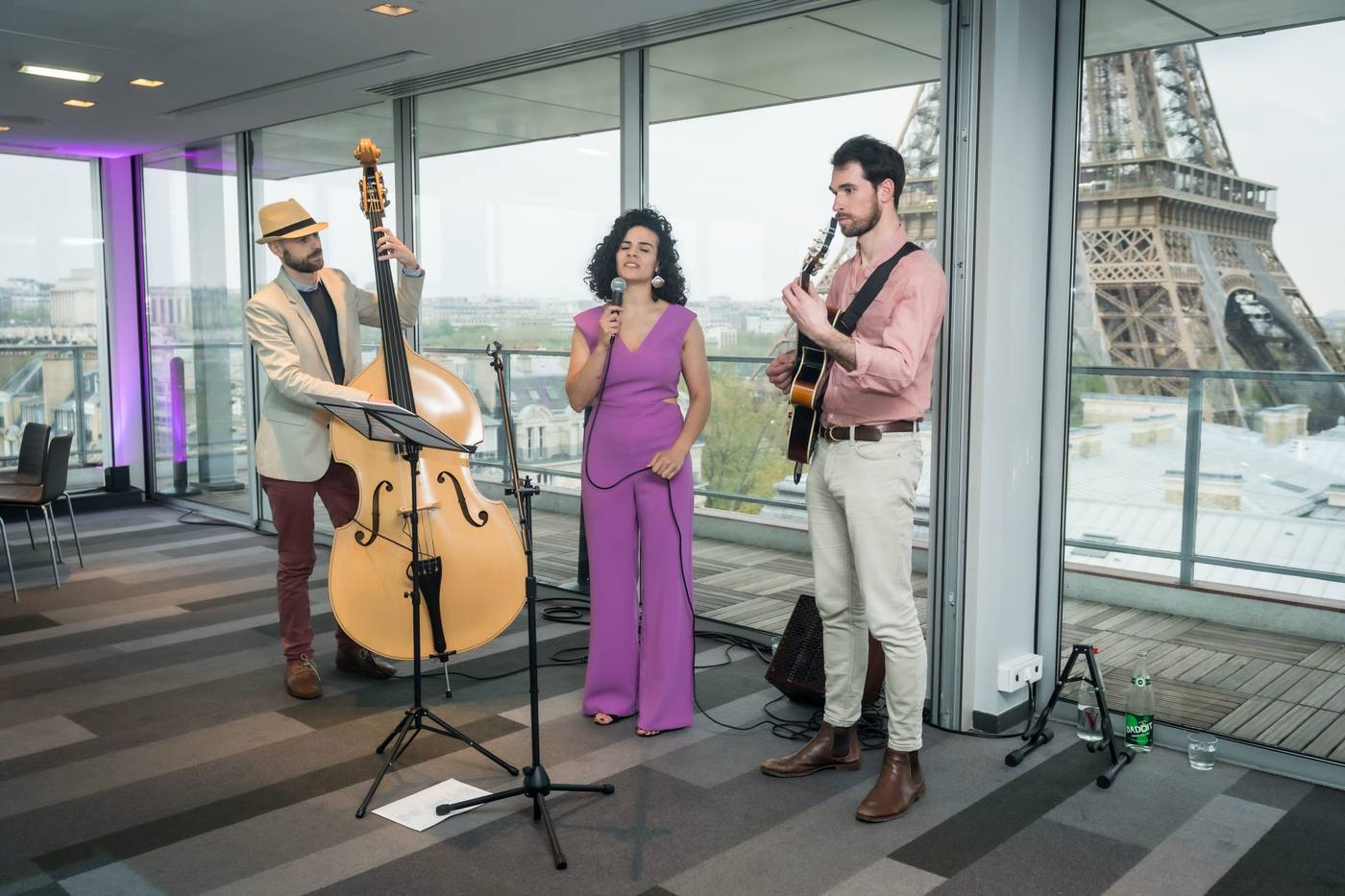 Trio de musiciens, contrebasse, chant et guitare, devant une baie vitrée donnant sur la tour Eiffel, pendant le séminaire international SVR organisé par Weevup