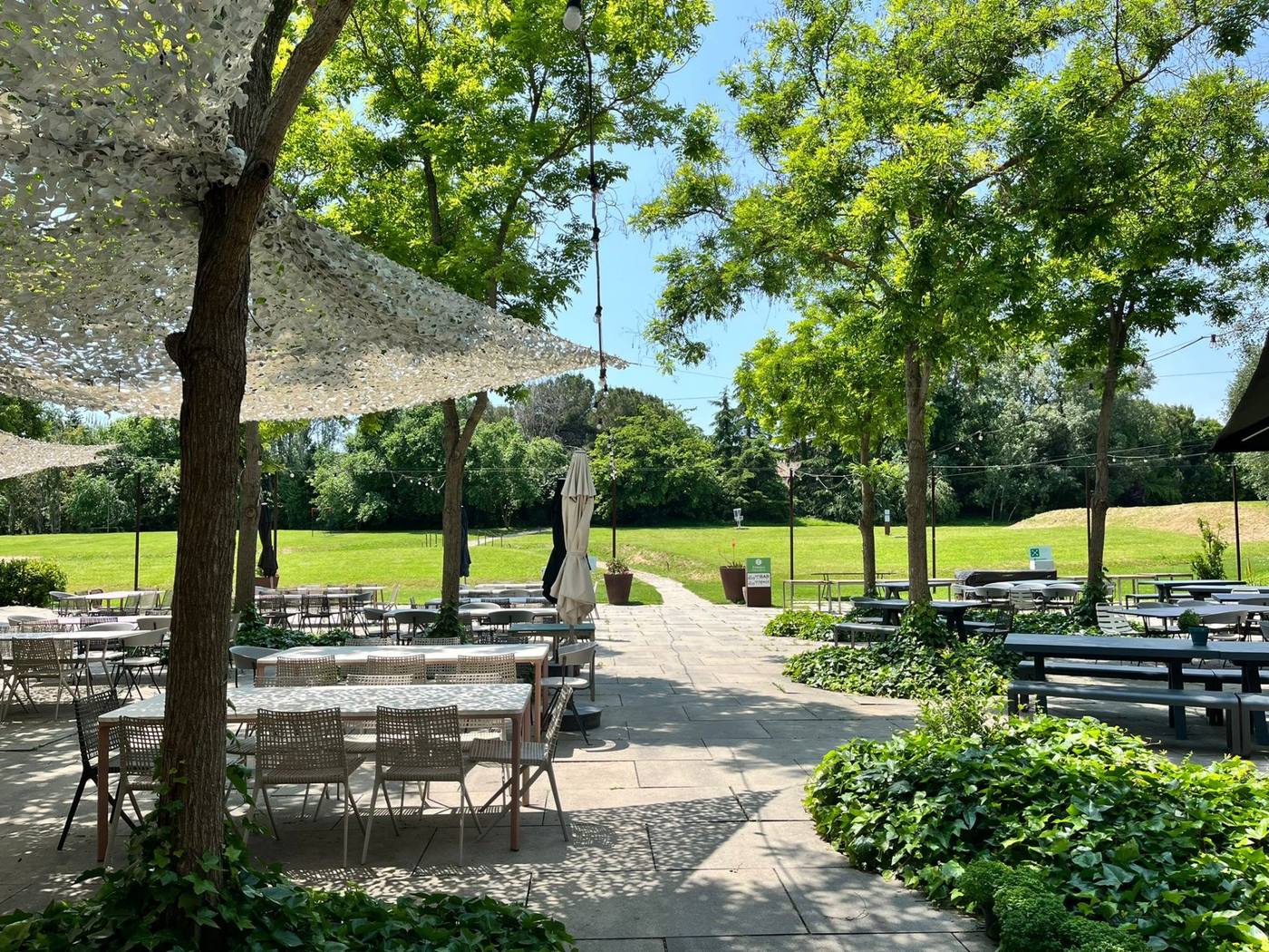 Terrasse ombragée aménagée avec tables et chaises sous de grands arbres, face à une pelouse, pendant le séminaire Cherry Ventures organisé par Weevup