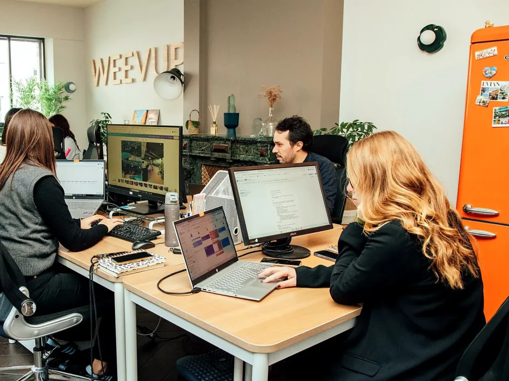 L’équipe Weevup au travail dans les bureaux de l’agence, au Vésinet (Yvelines), sous le logo Weevup en lettres de bois