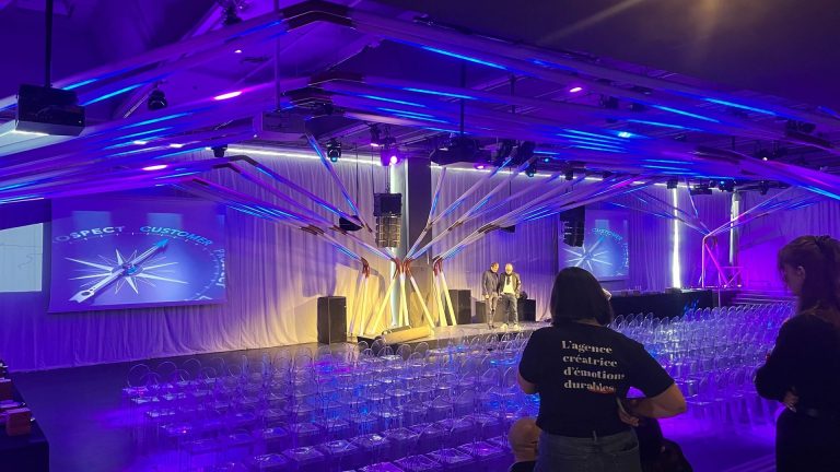 Salle plénière de la convention annuelle 3DS Outscale avant l’ouverture : chaises alignées face à la scène et aux écrans, sous une structure lumineuse