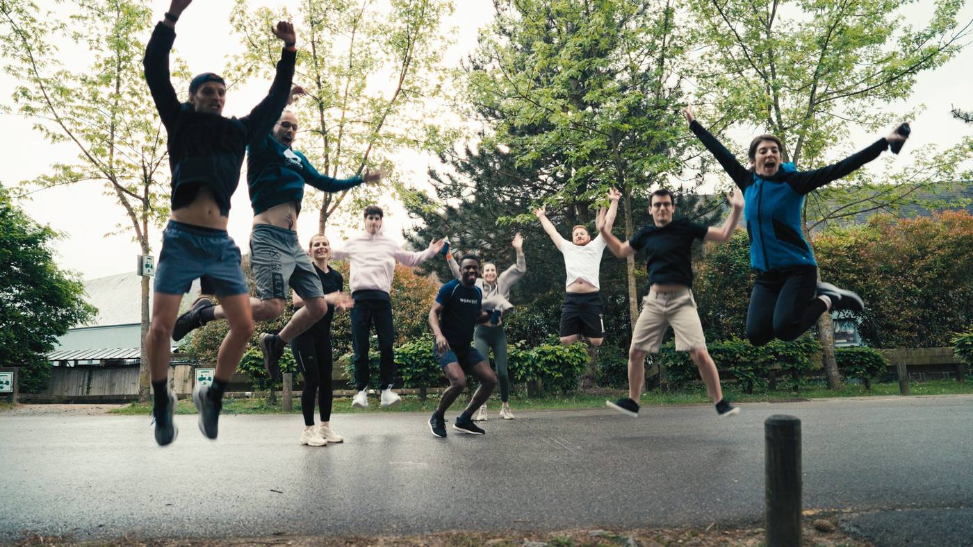 Collaborateurs de KPMG sautant ensemble en l'air sur une allée bordée d'arbres, pendant une activité sportive en extérieur de leur séminaire organisé par Weevup