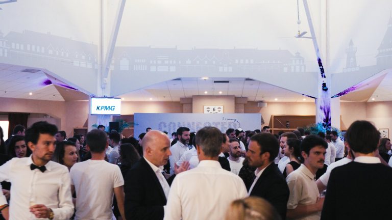 Collaborateurs de KPMG en tenue de soirée, nœud papillon pour certains, réunis debout sous une grande structure lumineuse pendant la soirée de leur séminaire