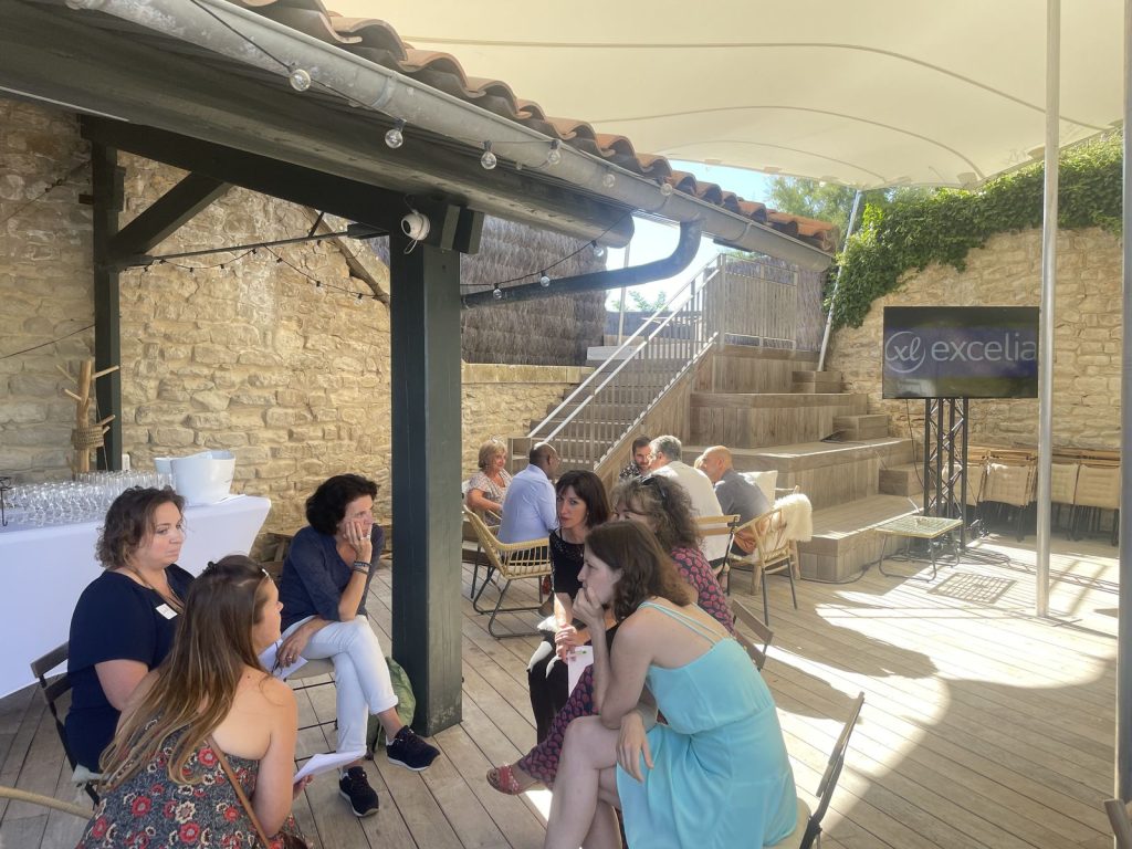 Petits groupes de collaborateurs d’Excelia en atelier près d’un écran au logo Excelia, entre murs de pierre et gradins en bois, au Bastion à Saint-Martin-de-Ré