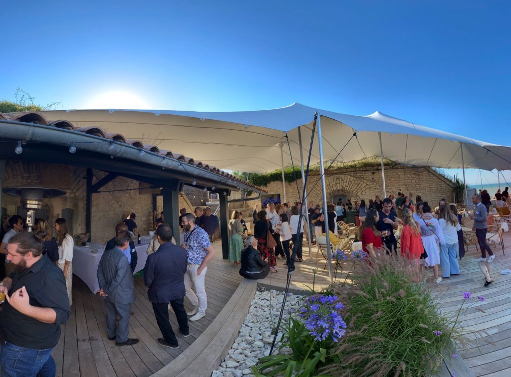 Cocktail en fin de journée sur la terrasse en bois du Bastion, collaborateurs d’Excelia sous la tente blanche et fleurs violettes au premier plan, sur l’île de Ré
