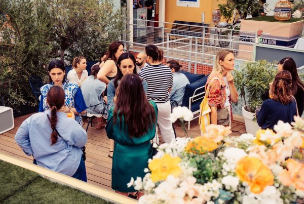 Invitées échangeant sur le rooftop de la cocktail party Dior organisée par Weevup, derrière une composition de fleurs blanches et orangées