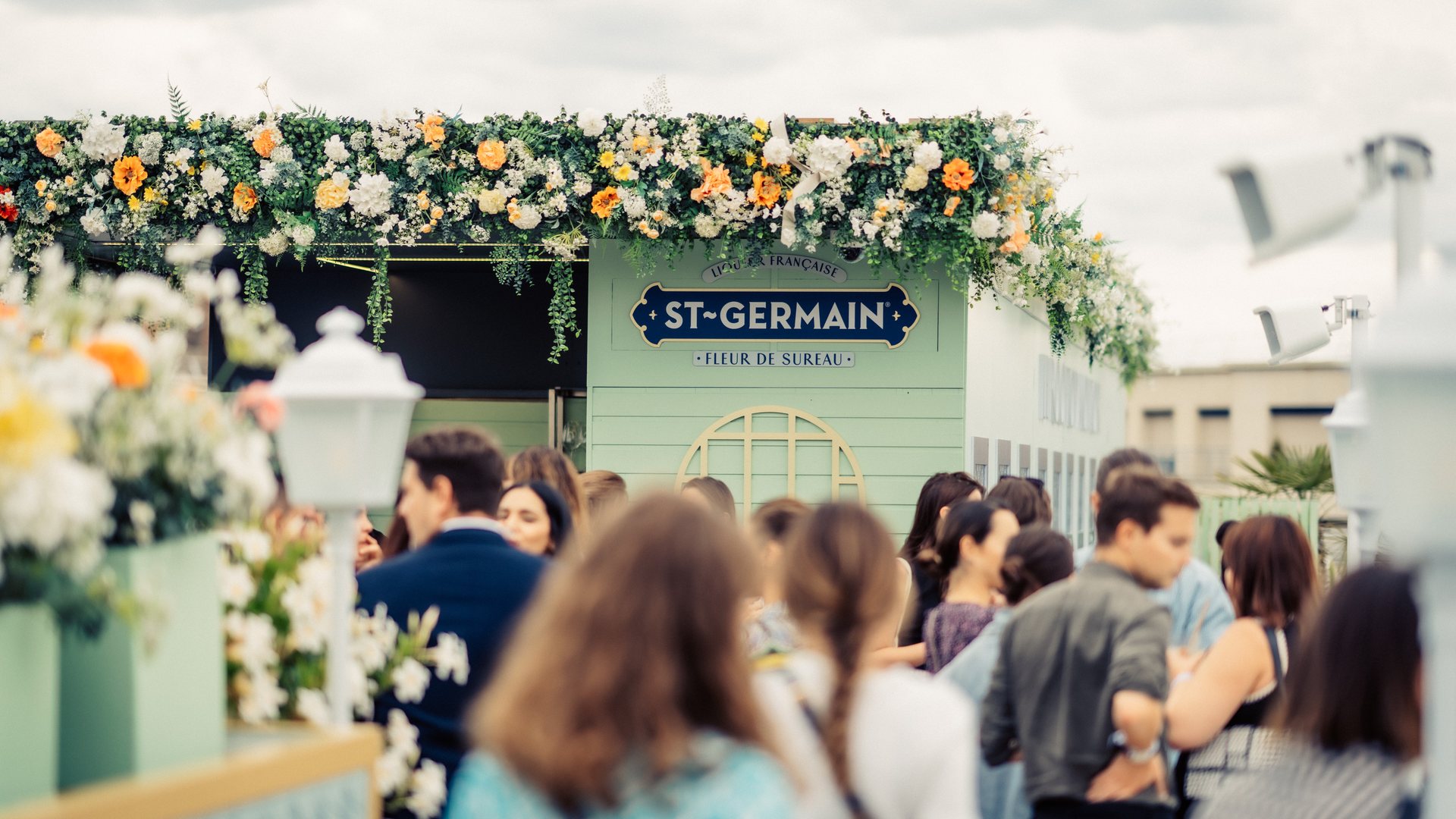 Invités du cocktail d'été de Dior devant un kiosque-bar St-Germain couronné de fleurs, lors de l'événement organisé par Weevup