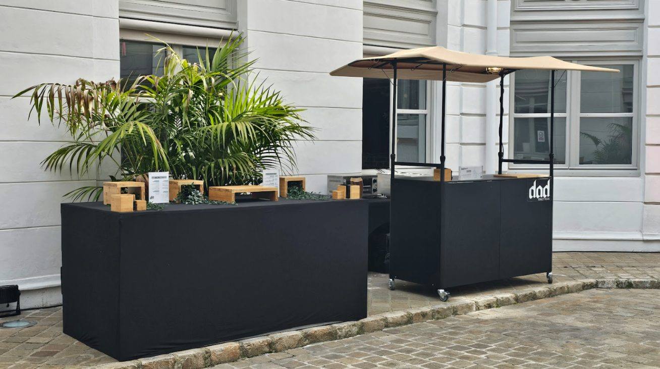 Stands du traiteur habillés de noir et décorés de plantes, installés sur les pavés d'une cour pour la Summer Party de Coty organisée par Weevup