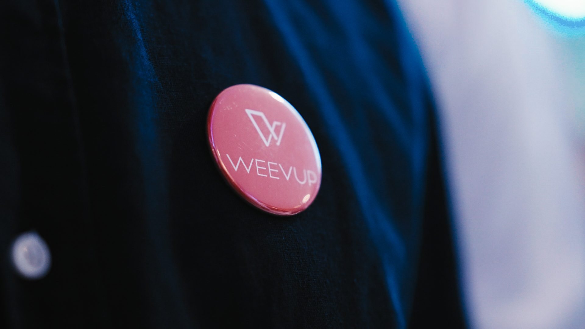 Badge rond rose corail au logo Weevup, épinglé sur un vêtement sombre, pendant le séminaire KPMG organisé par Weevup au Center Parcs du Lac d'Ailette