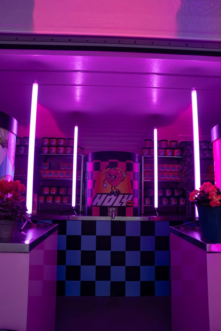 Intérieur de la remorque-bar Holy éclairé de néons roses, avec sa canette géante à robinet et ses étagères de canettes, au Lovely Brive Festival