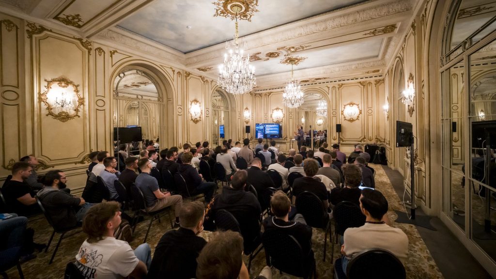 Plénière de la convention de janvier du Groupe Positive à Bruxelles, organisée par Weevup : participants assis face aux écrans dans un salon aux moulures dorées, sous des lustres en cristal