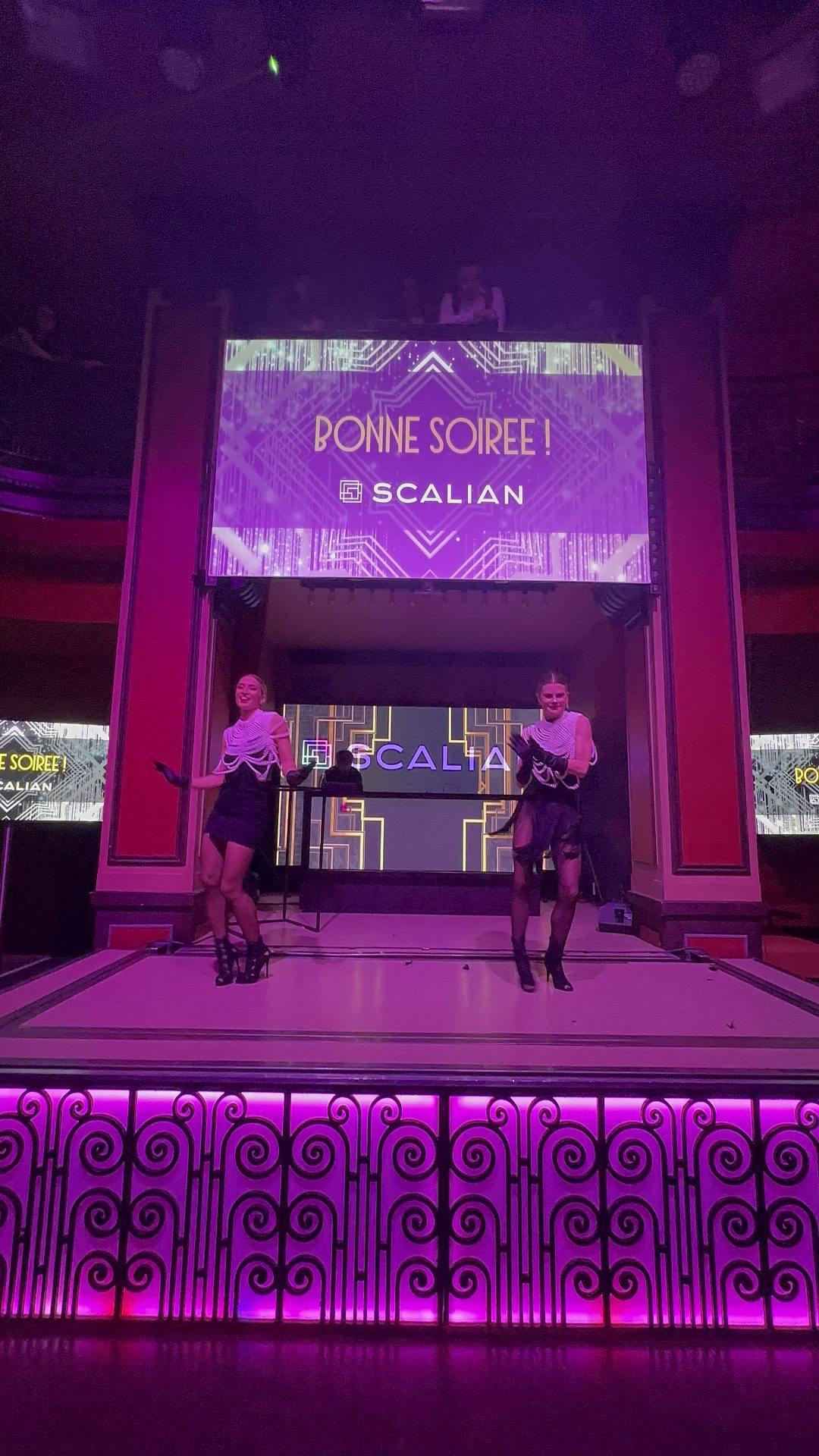 Deux danseuses en robe noire sur une scène éclairée de violet, sous un écran aux motifs Art déco affichant « Bonne soirée ! » et le logo Scalian, lors de la soirée awards organisée par Weevup