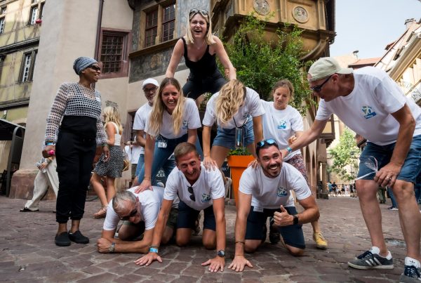 Collaborateurs d'Elanco en tee-shirts blancs formant une pyramide humaine dans une rue pavée du centre historique de Colmar, pendant le rallye connecté organisé par Weevup