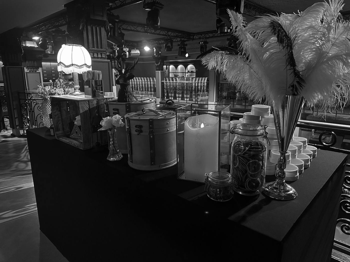 Table de buffet décorée pour la soirée années folles de Scalian : plumes d'autruche, lampe à franges, boîtes à chapeaux et bocaux d'agrumes séchés (photo en noir et blanc)