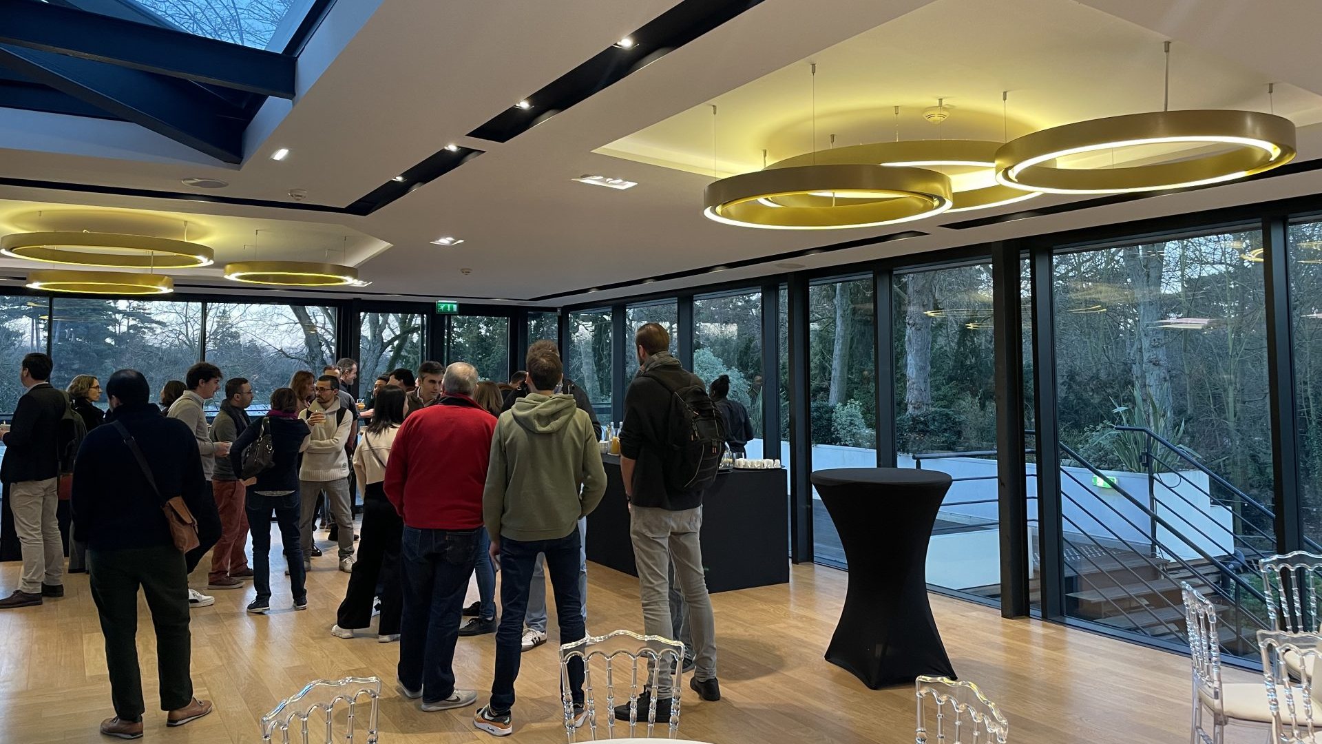 Participants réunis autour de mange-debout dans un pavillon vitré ouvert sur les arbres, sous de grandes suspensions dorées, pendant la convention annuelle 3DS Outscale organisée par Weevup au Pavillon Royal