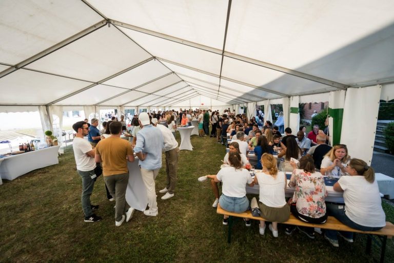 Collaborateurs d’Elanco réunis pour le déjeuner sous un grand chapiteau blanc, assis sur de longs bancs ou autour de mange-debout, pendant leur séminaire annuel organisé par Weevup