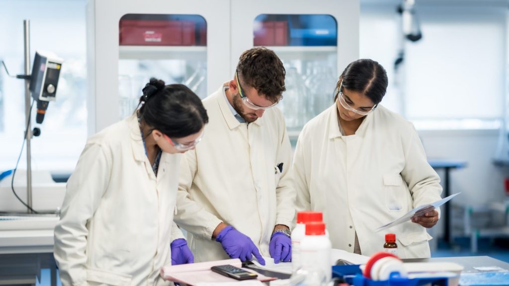 Collaborateurs d’Elanco en blouse blanche, lunettes et gants de protection, penchés sur un plan de travail dans un laboratoire du site de production, pendant leur séminaire annuel organisé par Weevup