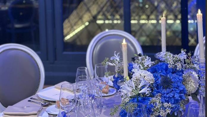 Table dressée de fleurs bleues et de bougies, avec vue de nuit sur la pyramide du Louvre, pour le dîner d'Iron Mountain auquel Weevup a contribué