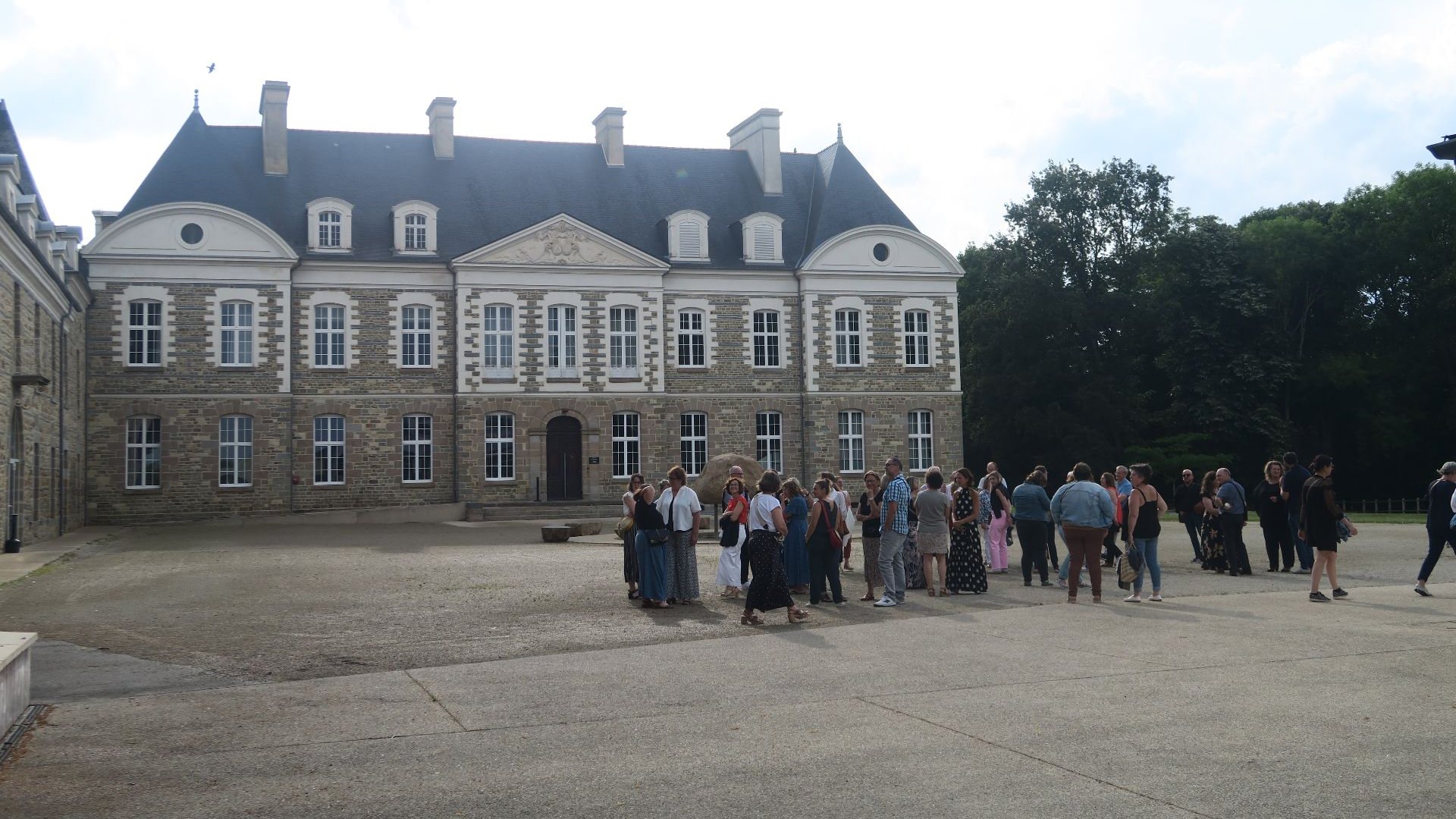 Invités de la soirée annuelle IGAM réunis dans la cour d'une demeure historique en pierre, bordée d'arbres, lieu choisi par Weevup pour réunir des équipes venues de plusieurs villes