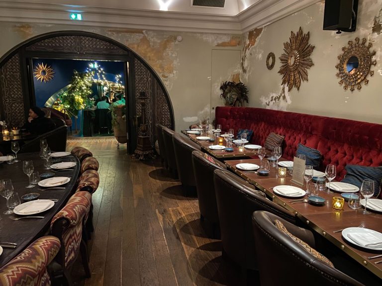 Longues tables dressées avec photophores, banquette de velours rouge et guirlandes lumineuses sous l’arche, pour le dîner de Norman K au Coya en décembre
