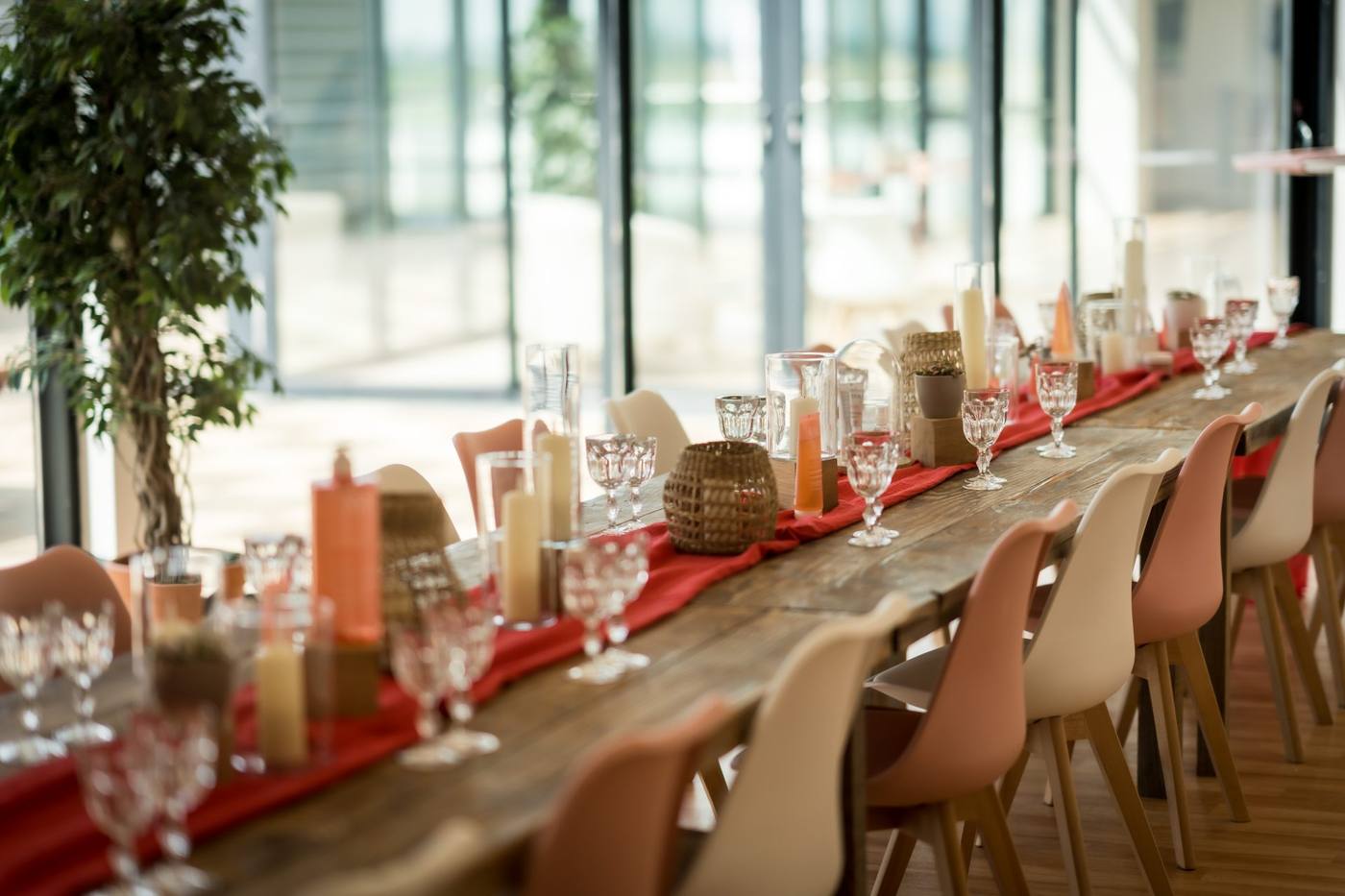 Longue table en bois dressée d'un chemin de table rouge, de verres et de photophores, devant de grandes baies vitrées, pour un repas du séminaire SVR