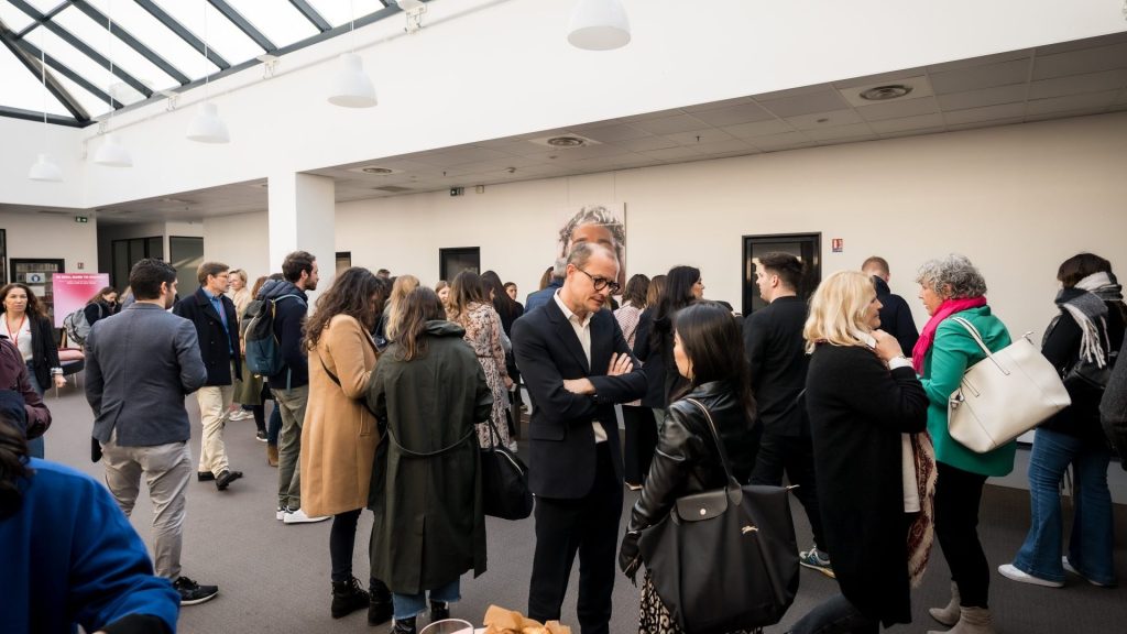 Participantes del seminario internacional de SVR, con abrigo y bolso al hombro, reunidos bajo la cristalera de un atrio en torno a un café de bienvenida