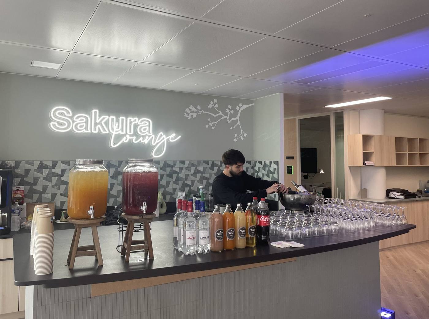 Barman derrière le comptoir du bar Sakura Lounge, avec fontaines de jus et verres alignés, pendant l'inauguration des nouveaux locaux de Daiichi organisée par Weevup