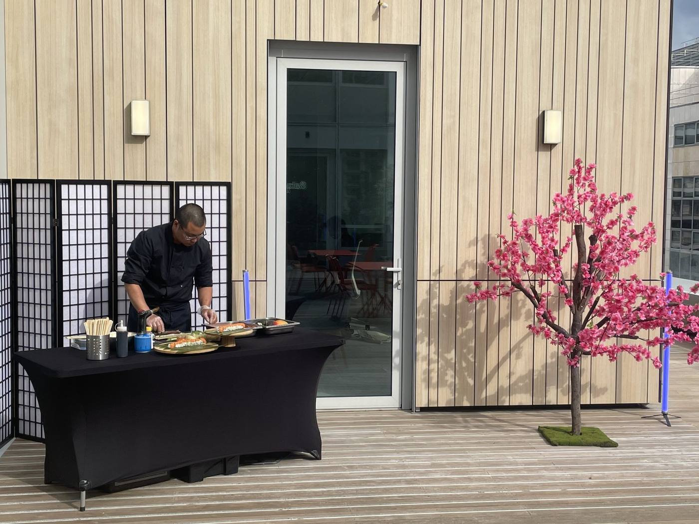 Maître sushi préparant ses plateaux sur une terrasse en bois, près d'un cerisier en fleurs et de paravents, lors de l'inauguration Daiichi organisée par Weevup