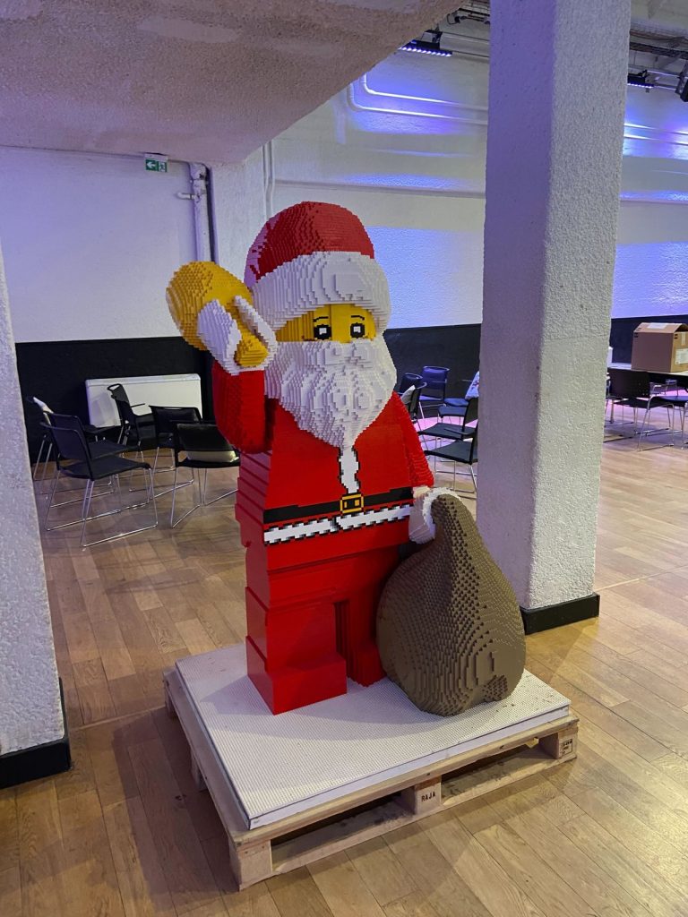 Père Noël géant en briques LEGO avec sa hotte et sa cloche dorée, installé pour le Noël solidaire de LEGO et Dons Solidaires