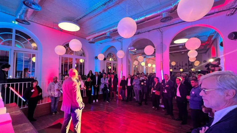 Prise de parole devant les invités de la soirée de lancement de marque de Groupe Atlantic, sous un éclairage rose et bleu et des suspensions en forme de globes