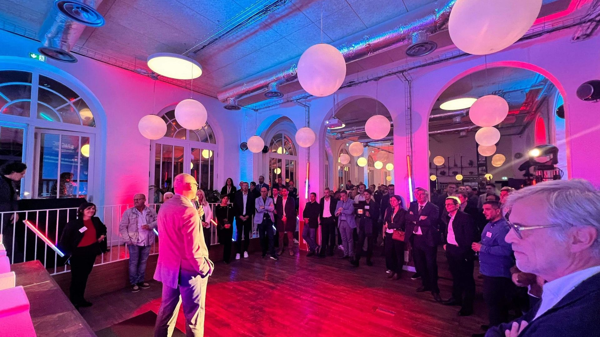 Prise de parole devant les invités de la soirée de lancement de marque de Groupe Atlantic, sous un éclairage rose et bleu et des suspensions en forme de globes