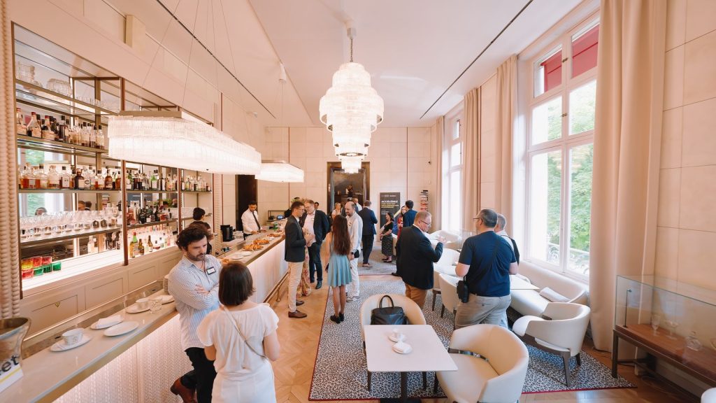 Invités autour du bar de la Maison Ducasse Baccarat, tasses de café et viennoiseries sur le comptoir, sous les lustres en cristal