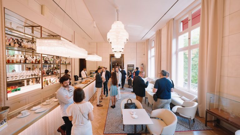 Invités de la journée clients Rimini Street autour du bar de la Maison Ducasse Baccarat, à Paris, tasses de café et viennoiseries sur le comptoir, sous les lustres en cristal