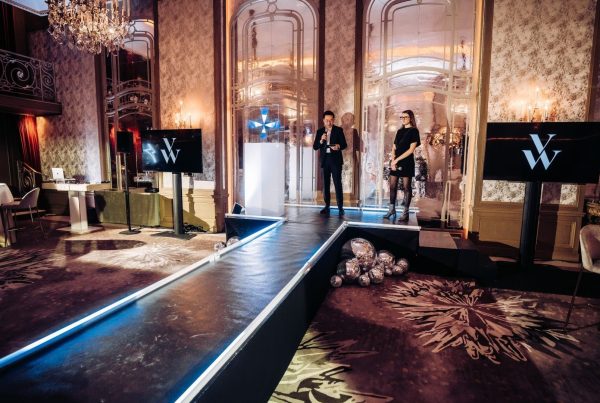 Podium bordé de LED bleues, écrans au logo de la marque et présentateurs sur scène, dans le salon à lustres aménagé par Weevup pour la soirée de lancement de produit de Vanessa Wu