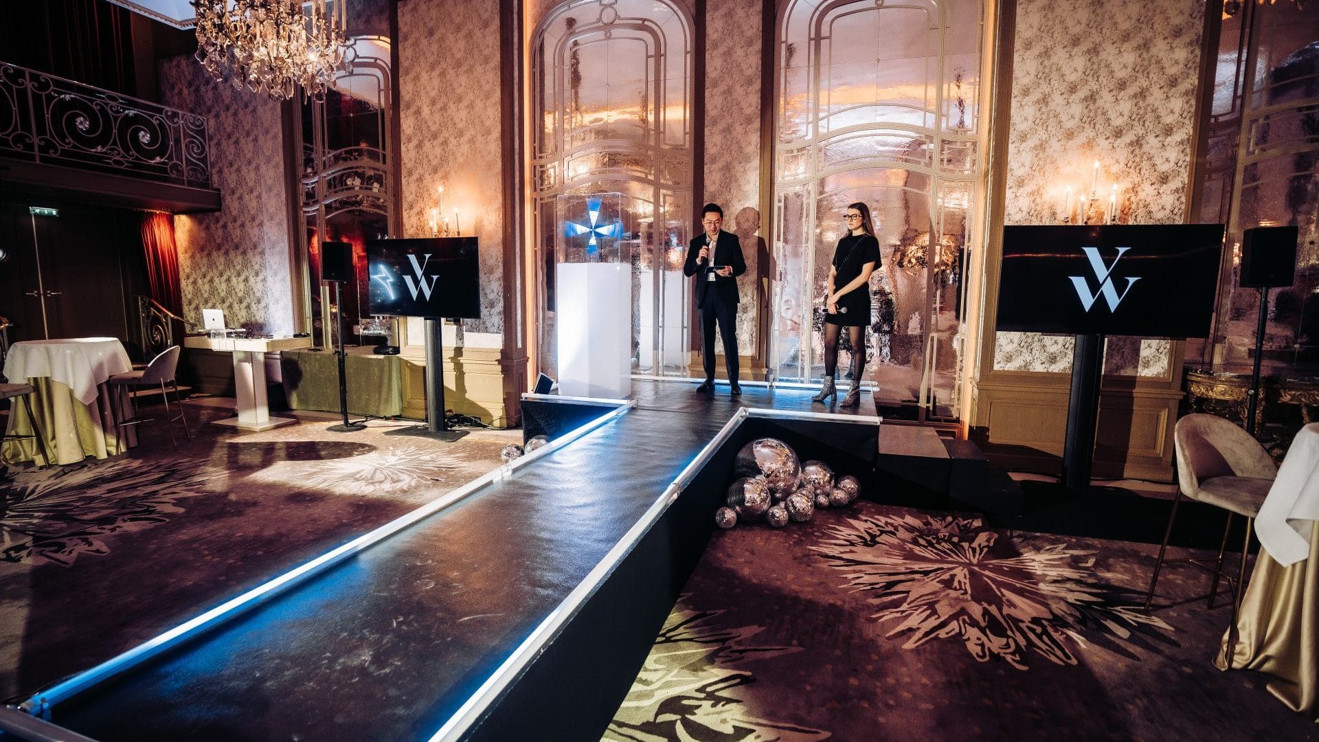 Podium bordé de LED bleues, écrans au logo de la marque et présentateurs sur scène, dans le salon à lustres aménagé par Weevup pour la soirée de lancement de produit de Vanessa Wu