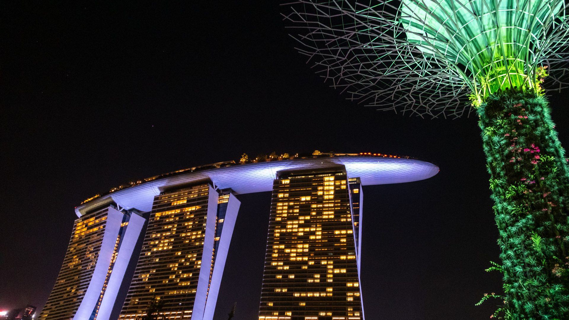 Hôtel aux trois tours illuminées reliées par un toit-terrasse et Supertree éclairé en vert, la nuit dans la baie de Marina à Singapour, destination de séminaire en Asie