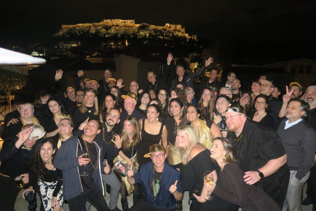Participants du séminaire de Bio-Rad en tenue noire et accessoires dorés sur la terrasse du Muse Urban, avec l'Acropole illuminée en arrière-plan, à Athènes.
