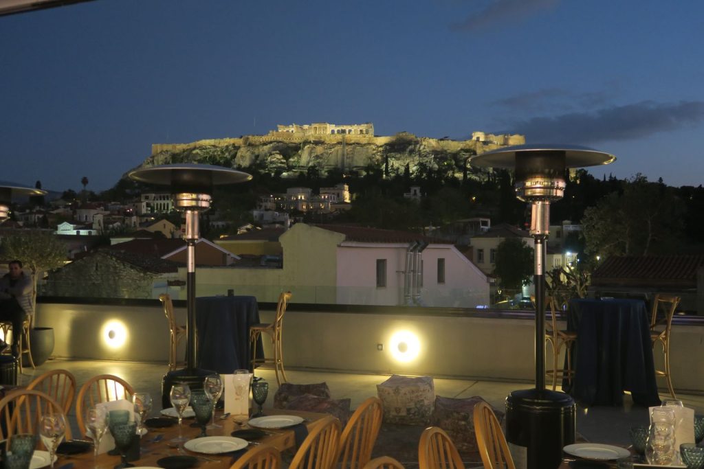 Terrasse du Muse Urban dressée pour la soirée de gala de Bio-Rad, chaises en bois et parasols chauffants, face à l’Acropole illuminée à la tombée de la nuit