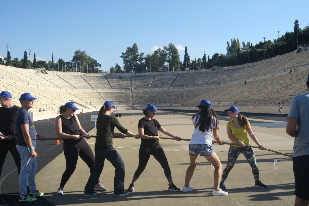 Participants en casquette bleue au tir à la corde, devant les gradins de marbre du stade panathénaïque, pendant le séminaire de Bio-Rad