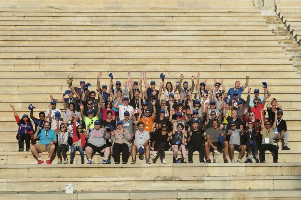 Photo de groupe des participants de Bio-Rad, médailles au cou et casquettes levées, dans les gradins de marbre du stade panathénaïque