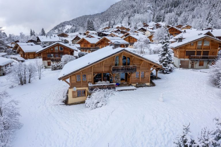 Chalets en bois sous la neige, au pied d’une montagne boisée, dans une station de ski des Alpes
