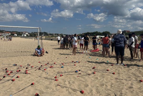 Collaborateurs de MYM réunis sur une plage de Biarritz autour d'un animateur, avant des jeux d'équipe inspirés de Koh Lanta, pendant leur séminaire organisé par Weevup