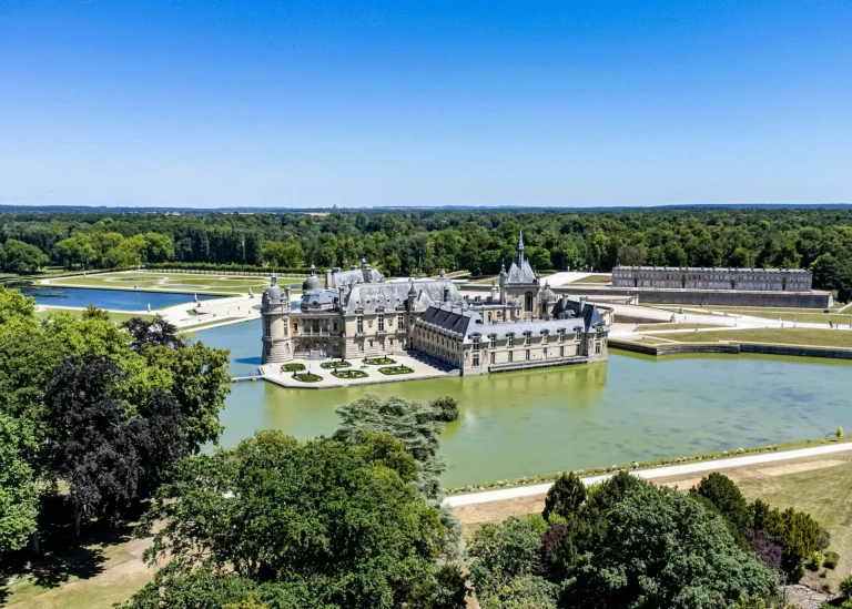 Le Château de Chantilly entouré d’eau, avec ses jardins et la forêt à l’horizon, vu du ciel