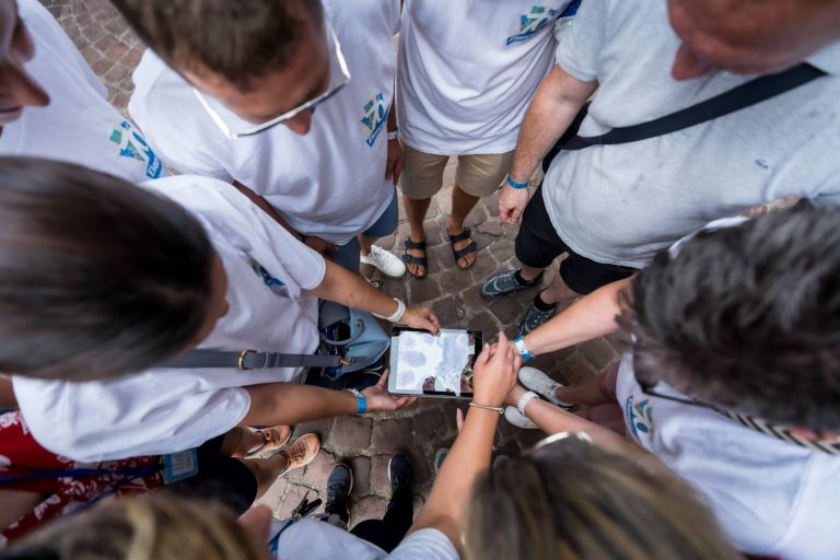 Collaborateurs d’Elanco en tee-shirts blancs réunis en cercle autour d’une tablette, sur les pavés de Colmar, pendant le rallye connecté de leur séminaire annuel