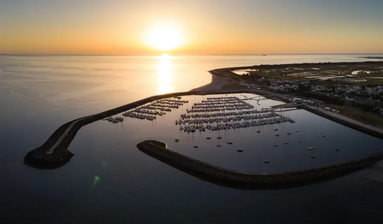 Un port de l’île de Noirmoutier vu du ciel au coucher du soleil, ses bateaux à l’abri des digues face à l’océan